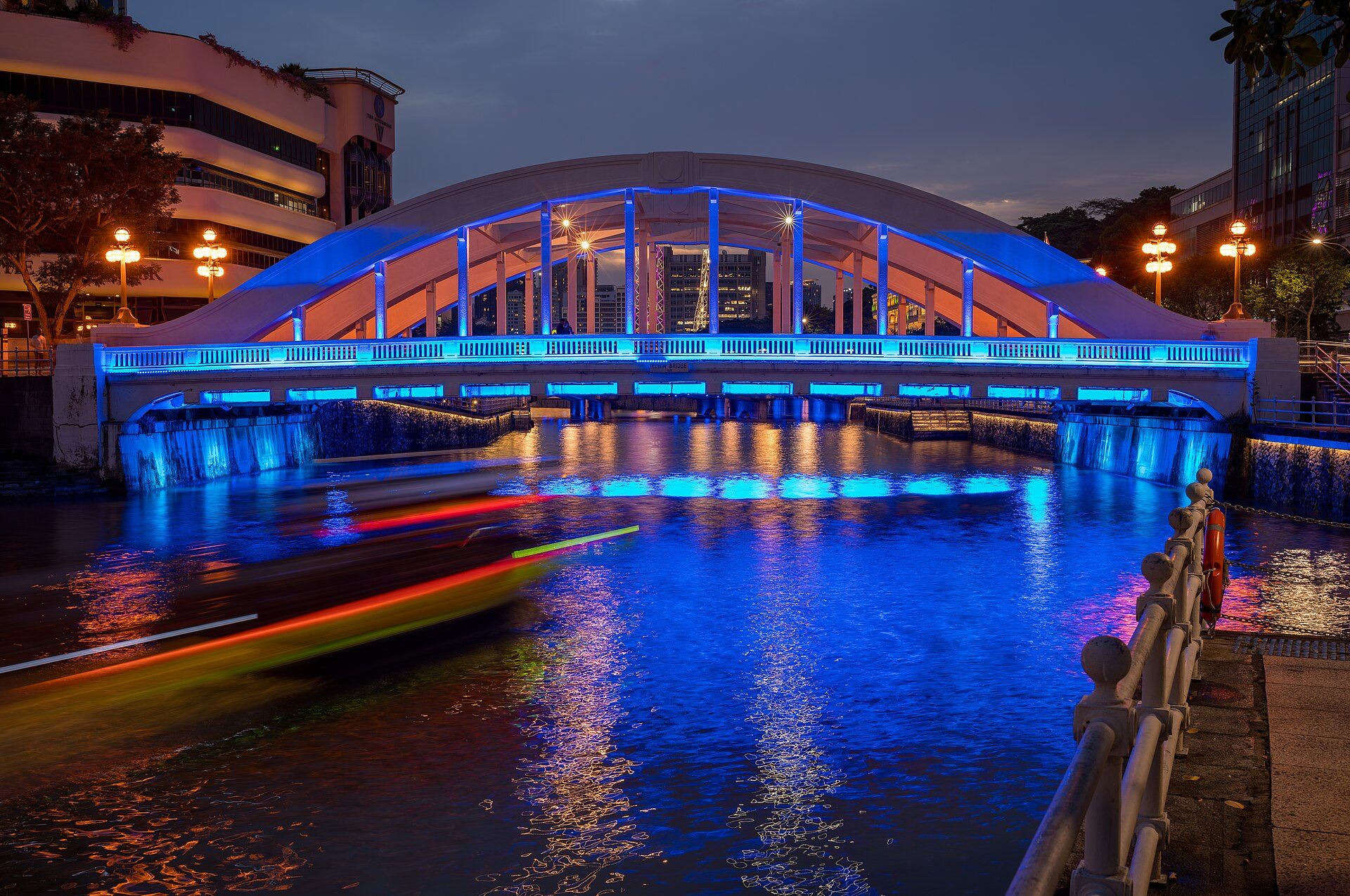 Elgin Bridge lit up over the Singapore River at dusk, with a boat passing beneath it